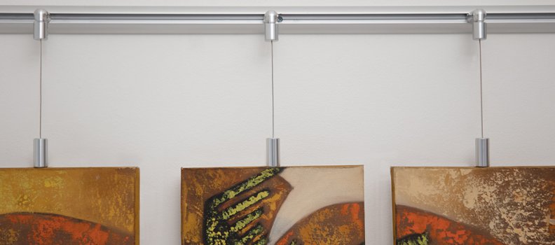 Adjustable WS-Wall Track & Wire Connectors hang gallery wrapped art to keep walls pristine. This installation is achieved with an HD-CBS1 Combination screw fastened to the wooden frame and connected to the wire with a WS-A27B Wire Mount. Optional lengths of 3/64” wire then connect up to the WS-A26B Hinged Top Extrusion Mount. Finally, the wire system is attached to the wall with the SL-WT Wall Track Extrusion. Wall track can be installed on the ceiling where applicable or use the WS-A1B Ceiling Mounts.